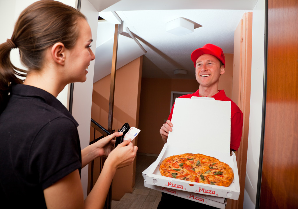 delivery boy lifting the cover of the pizza for the customer to see