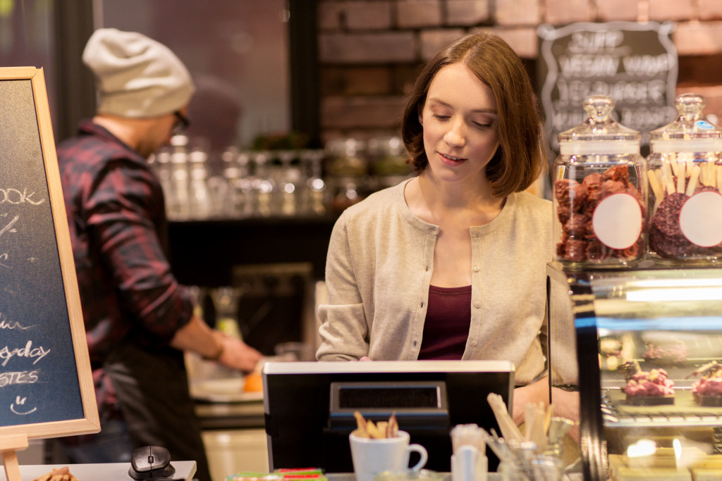 small business, people and service concept - woman or bartender at cafe or coffee shop counter with cashbox